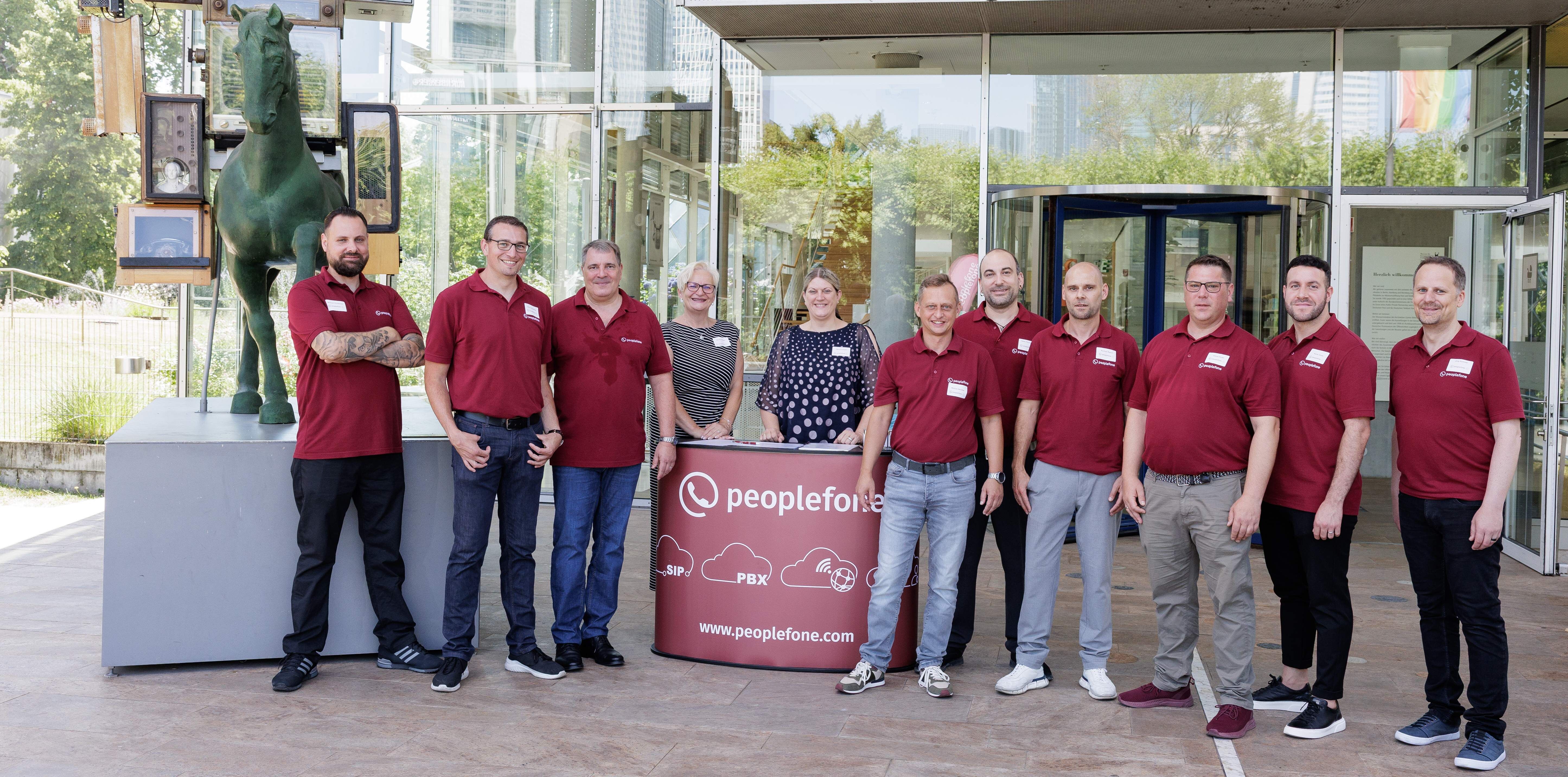 peoplefone Mitarbeiter stehen vor dem Eingang vom Museum für Kommunikation um einen roten Tisch.