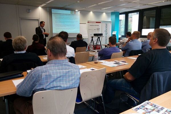 Tischreihen mit peoplefone Partnern, die einem Referenten zuhören, der vor einer Bildschirmleinwand steht.