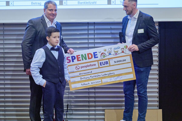 Drei Personen halten auf der Bühne einen Spendenscheck in der Hand.