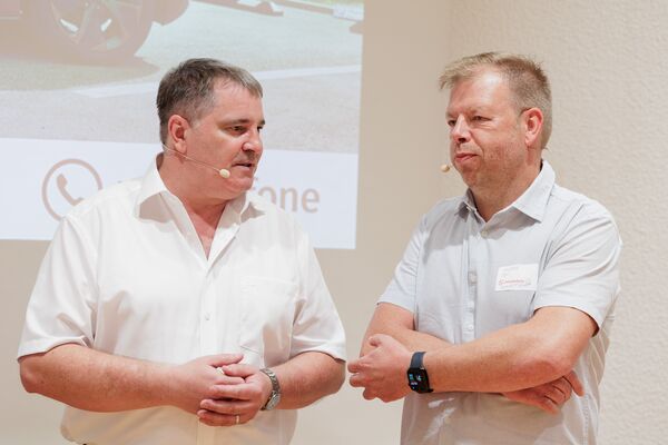 Zwei Personen stehen vor einer Leinwand mit Headset und führen ein Gespräch.