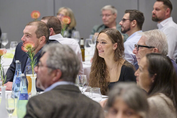 Personen sitzen im Raum an runden Tischen zusammen und reden.