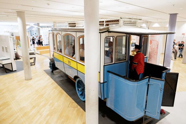 Alter Postwagen in Ausstellung mit Personen darin.
