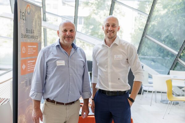 Zwei Personen stehen an einem Messestand und schauen in die Kamera.