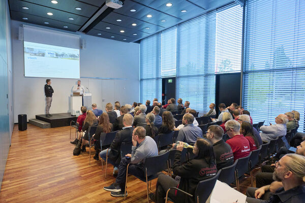 Zuschauer sitzen auf Stühlen in Richtung Bühne und hören einem Vortrag zu.