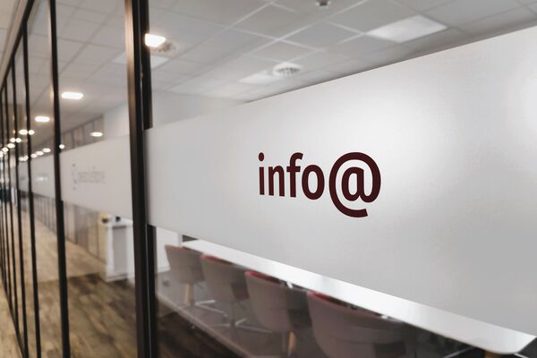 Glaswand mit Blick in ein Büro. Aufkleber mit der Aufschrift info@ im Vordergrund.