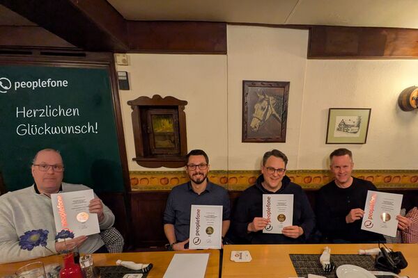 Vier Personen sitzen mit Urkunden in der Hand auf einer Holzbank.