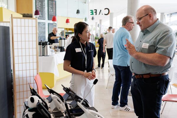 Menschen stehen an Ständen und unterhalten sich in kleinen Gruppen.