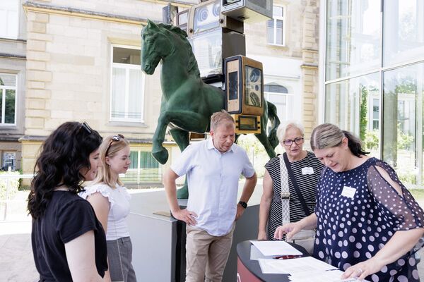 Personen vor dem Eingang registrieren sich an einem Tisch.