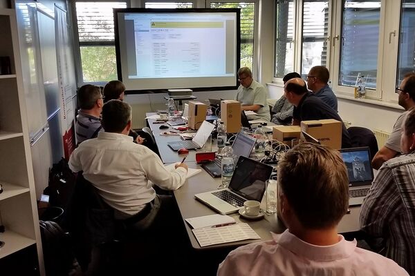 peoplefone Partner an einem Tisch sitzend schauen auf eine Bildschirmleinwand und hören dem Referenten zu.