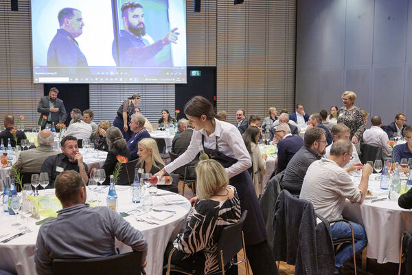 Personen sitzen im Raum an runden Tischen zusammen und reden.