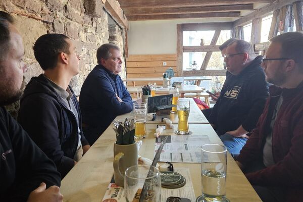 Personen sitzen an einem langen Tisch und unterhalten sich.
