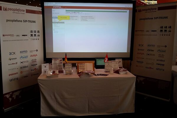 Blick auf peoplefone Messestand mit Bildschirmleinwand und zwei Bannern.