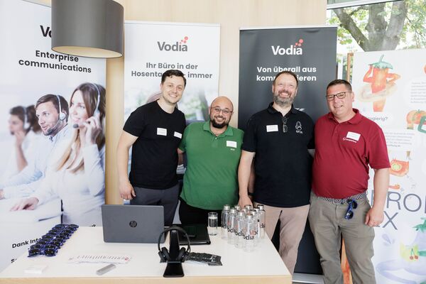 Vier Personen stehen vor mehreren Bannern und schauen in die Kamera.