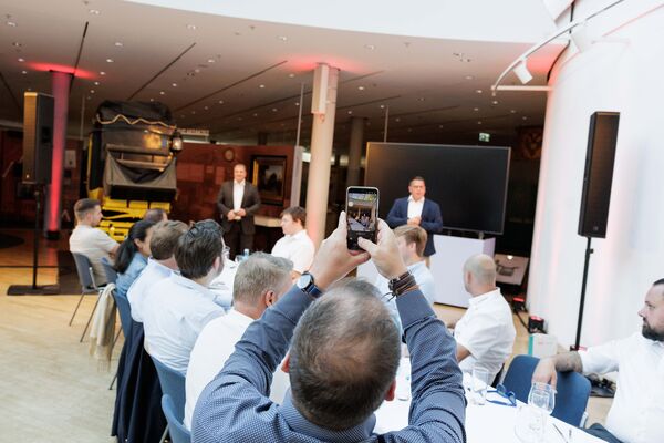 Mehrere Personen sitzen an Tischen im Lichthof, essen und unterhalten sich. Teile der Ausstellung sind im Hintergrund sichtbar.