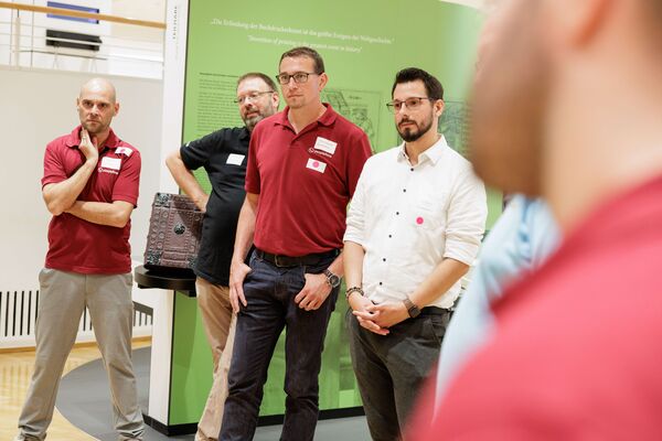 Mehrere Personen stehen in der Ausstellung und hören zu.