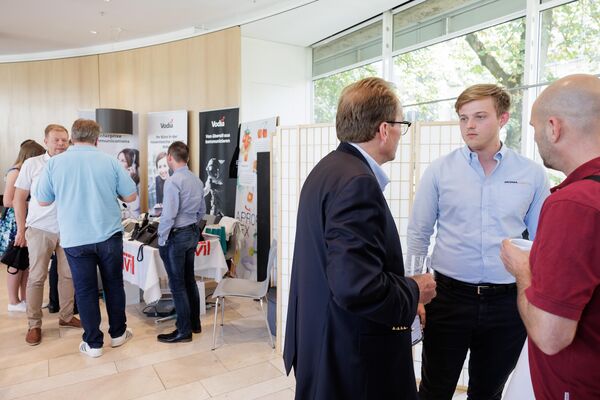 Menschen stehen an Ständen und unterhalten sich in kleinen Gruppen.