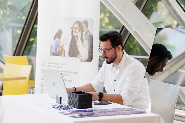 Eine Person sitzend am Messestand arbeitet am Laptop.