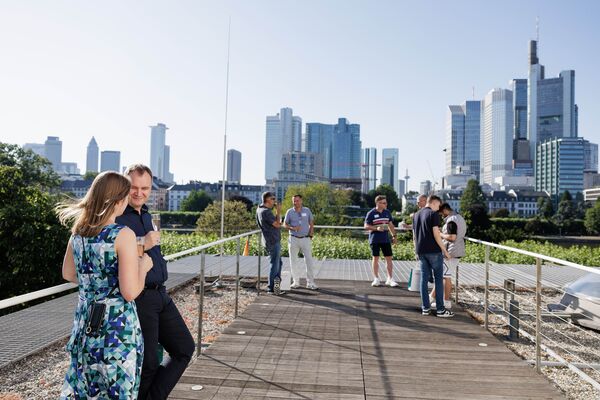 Mehrere Personen stehen auf einer Dachterrasse. Im Hintergrund ist die Skyline von Frankfurt zu sehen.