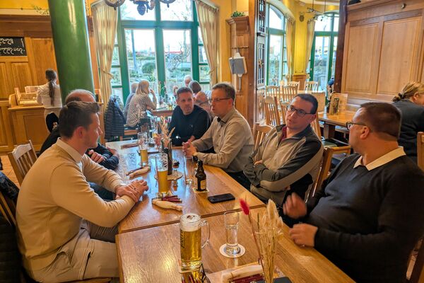 Personen sitzen an einem langen Holztisch und unterhalten sich.