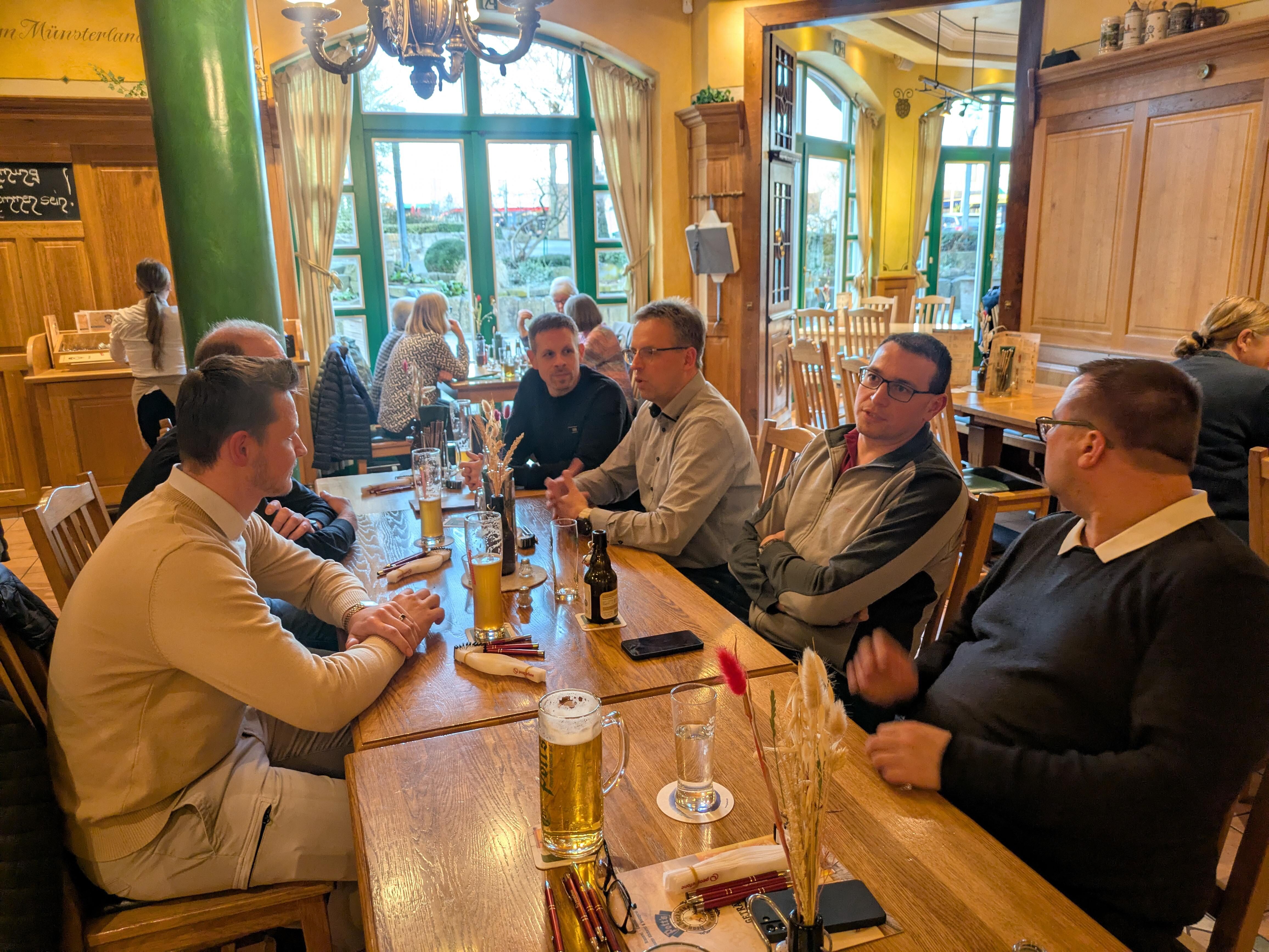 Personen sitzen an einem langen Holztisch und unterhalten sich.
