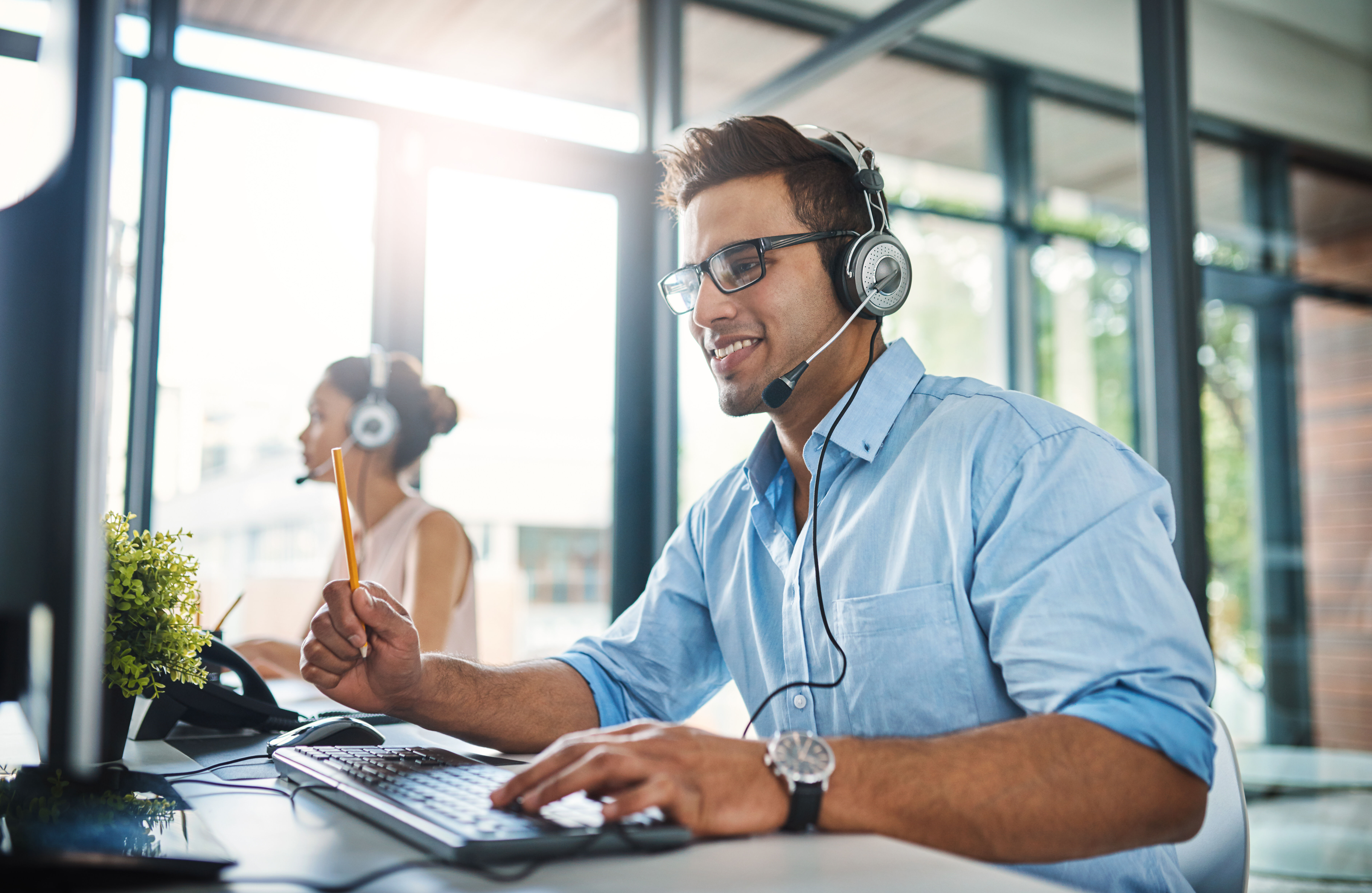 Männliche Person sitzt mit Headset in einem Call Center.