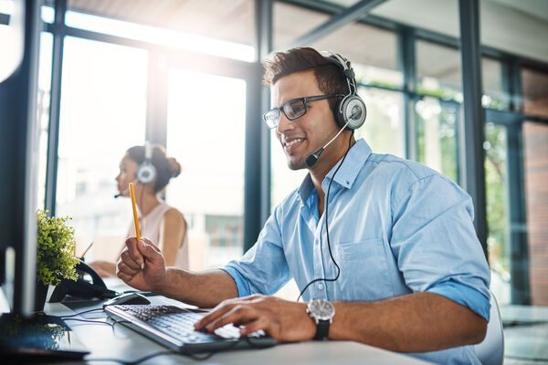 Männliche Person sitzt mit Headset in einem Call Center.