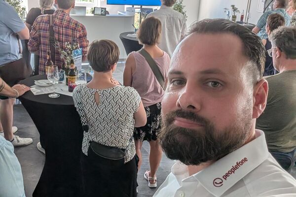 Person macht Selfie während eines Vortrags. Weitere Personen sind von hinten zu sehen.