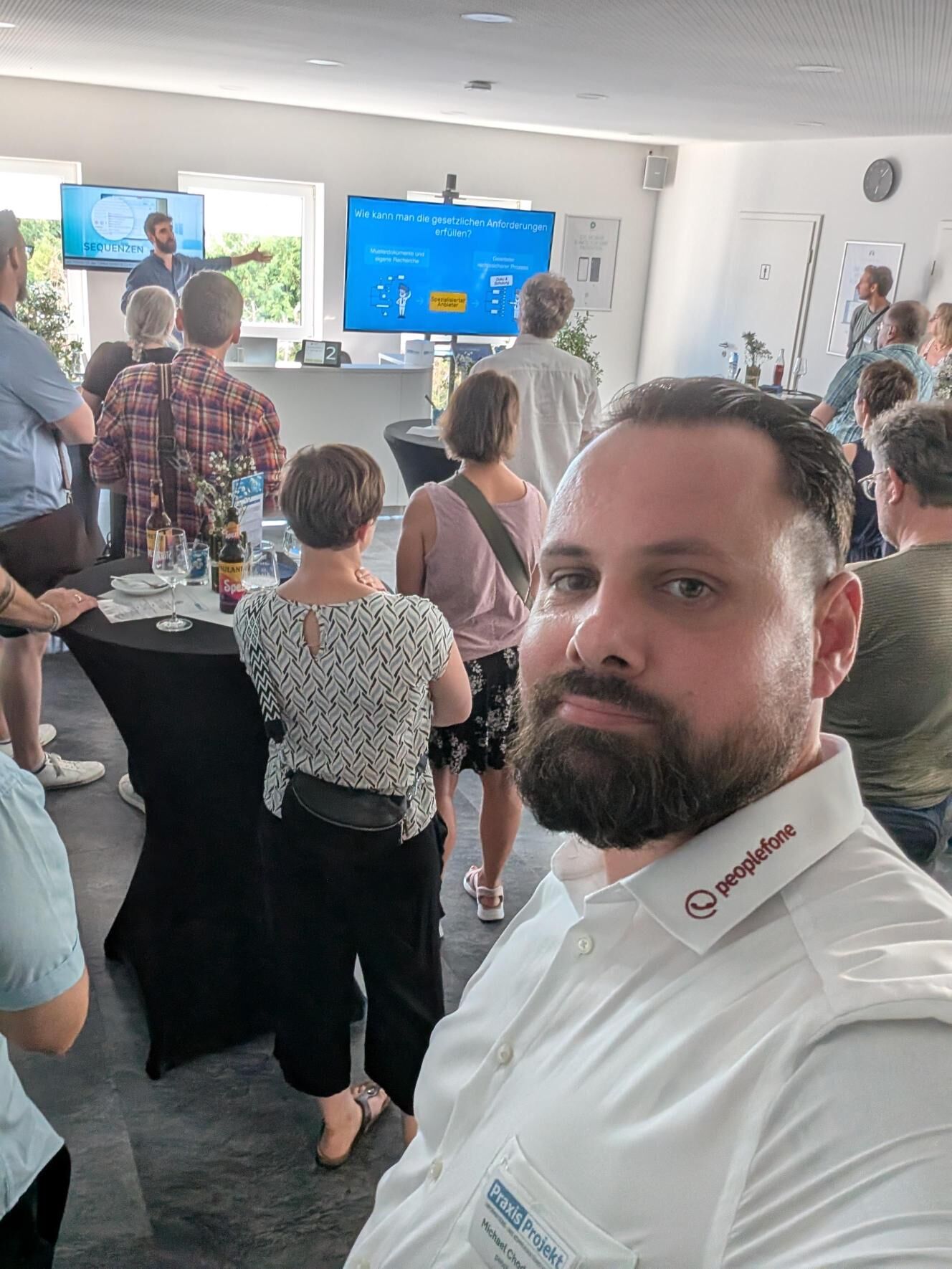 Person macht Selfie während eines Vortrags. Weitere Personen sind von hinten zu sehen.