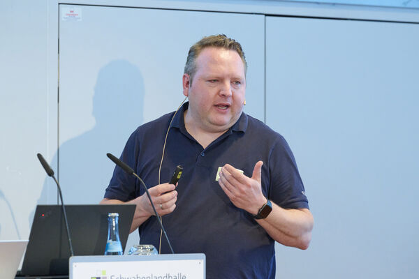 Eine Person steht auf der Bühne mit Mikrofon und hält einen Vortrag.