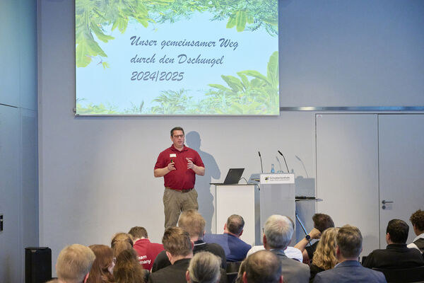 Eine Person steht auf der Bühne mit Mikrofon und hält einen Vortrag.