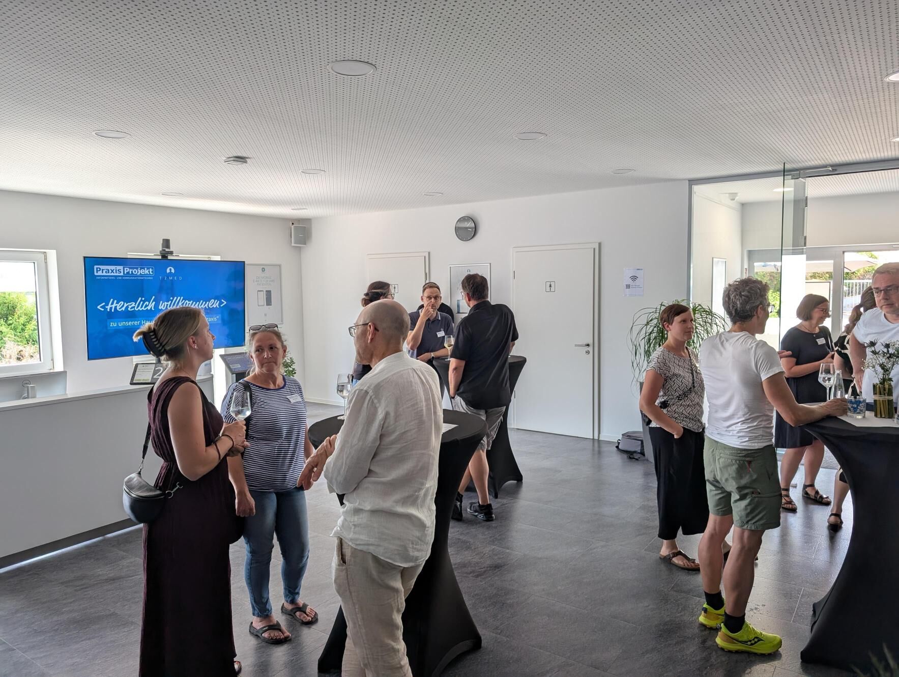 Mehrere Personen stehen an Stehtischen in einem Ausstellungsraum und unterhalten sich.