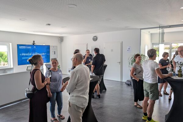 Mehrere Personen stehen an Stehtischen in einem Ausstellungsraum und unterhalten sich.