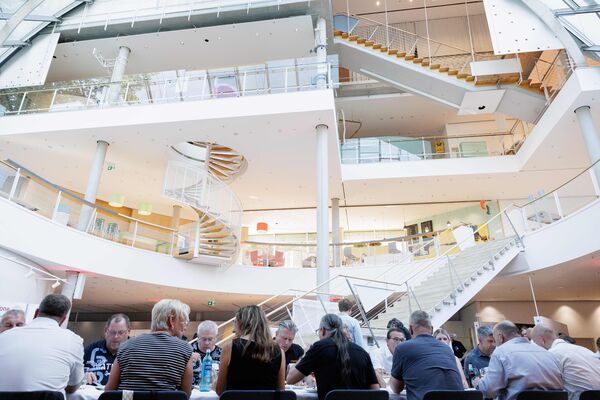 Mehrere Personen sitzen an Tischen im Lichthof, essen und unterhalten sich. Teile der Ausstellung sind im Hintergrund sichtbar.