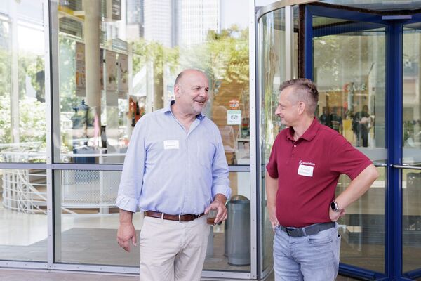 Zwei Personen stehen vor einem Eingang und unterhalten sich.