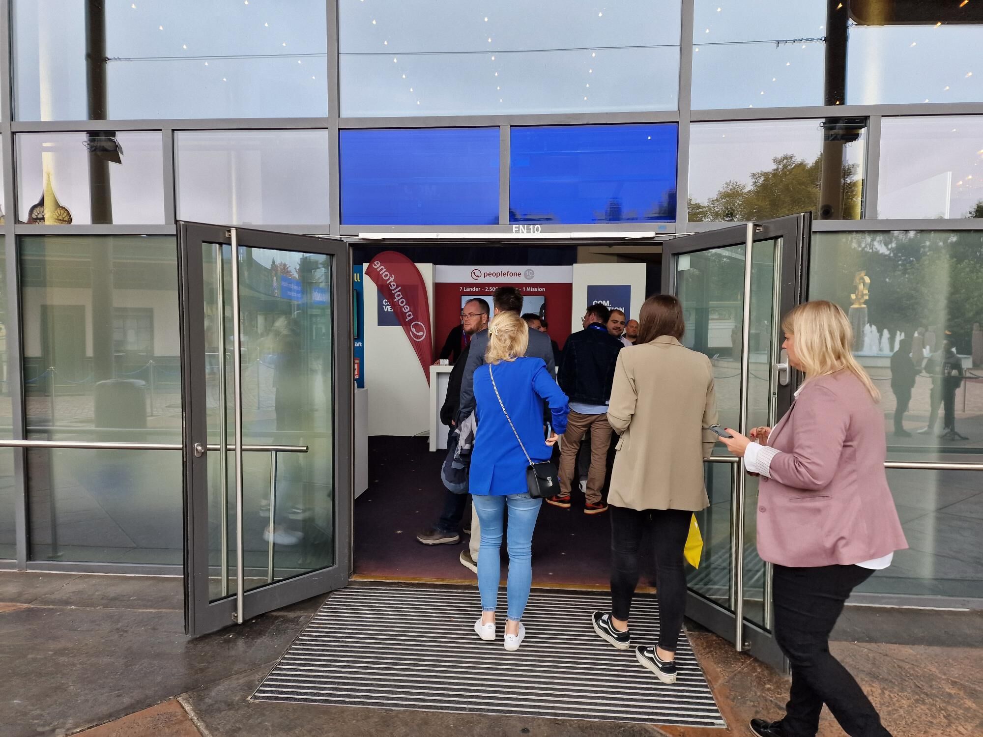 Mehrere Personen gehen durch einen Messeeingang auf einen Stand zu.