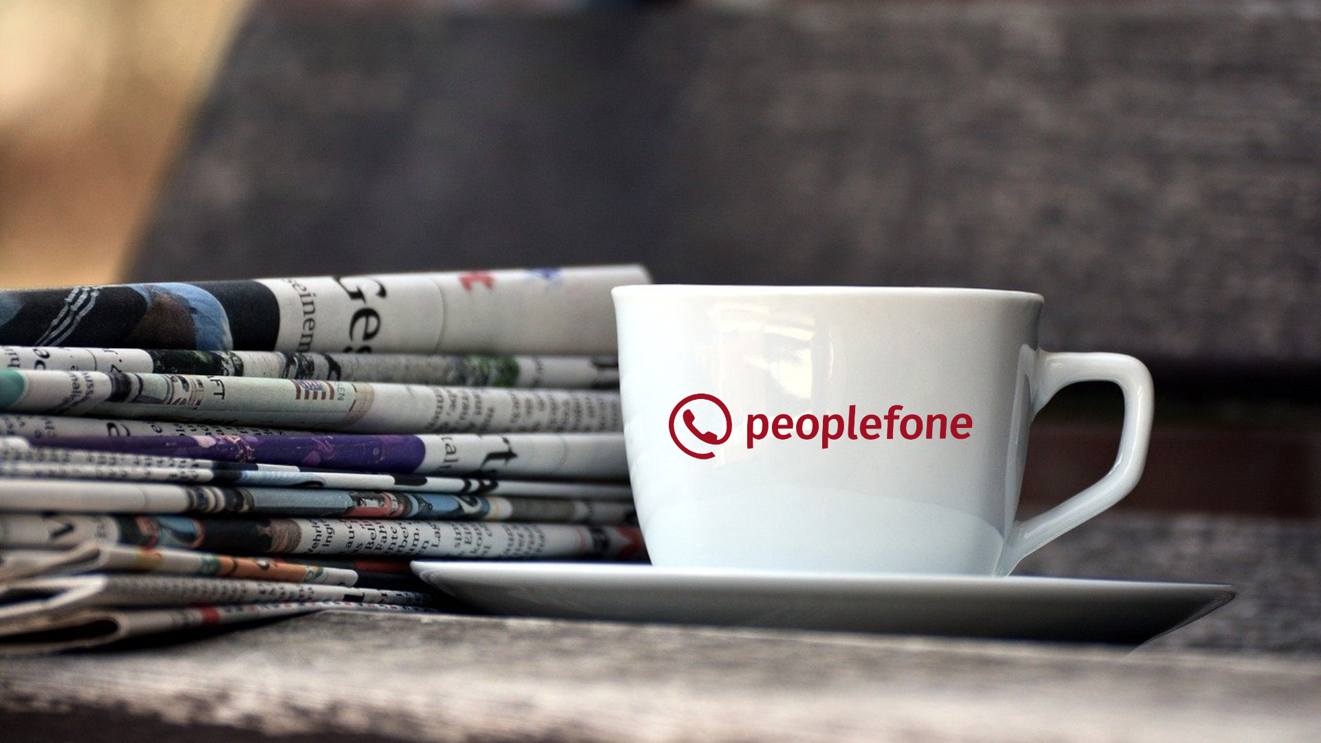 Kaffeetasse mit peoplefone-Logo vor einem Zeitungsstapel.
