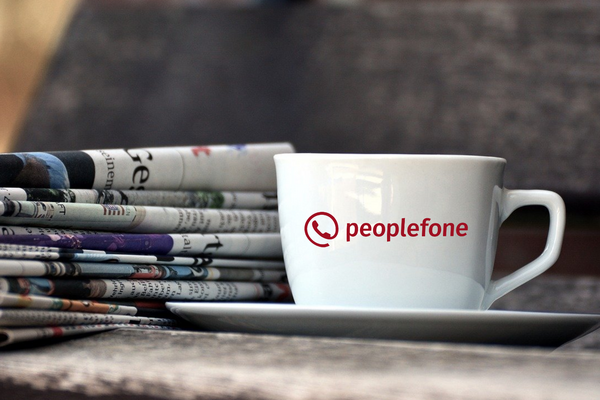 Kaffeetasse mit peoplefone-Logo vor einem Zeitungsstapel.