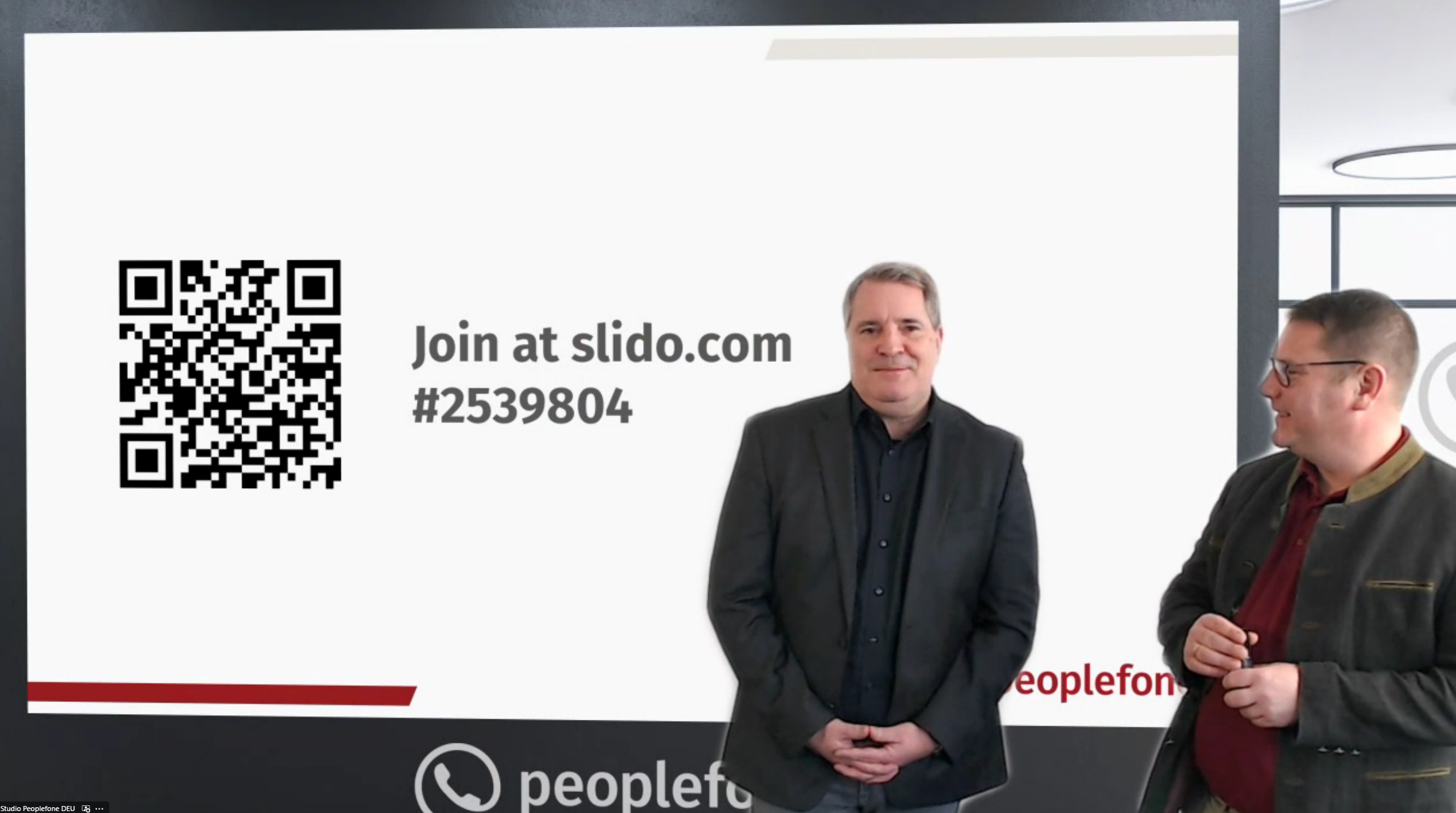 Zwei Personen stehen vor einer Präsentationswand, auf der ein QR-Code abgebildet ist für eine Abstimmung.