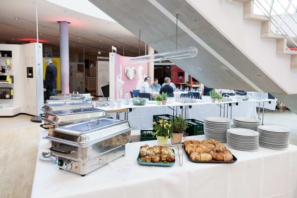 Mehrere Personen sitzen an Tischen im Lichthof, essen und unterhalten sich. Teile der Ausstellung sind im Hintergrund sichtbar.